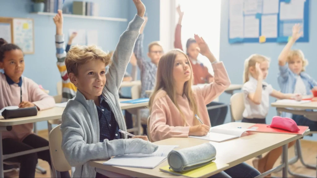 School security guard services ensure student safety – American Security Force Elementary school students raising hands in a classroom, highlighting the importance of school security guard services for student safety – American Security Force.