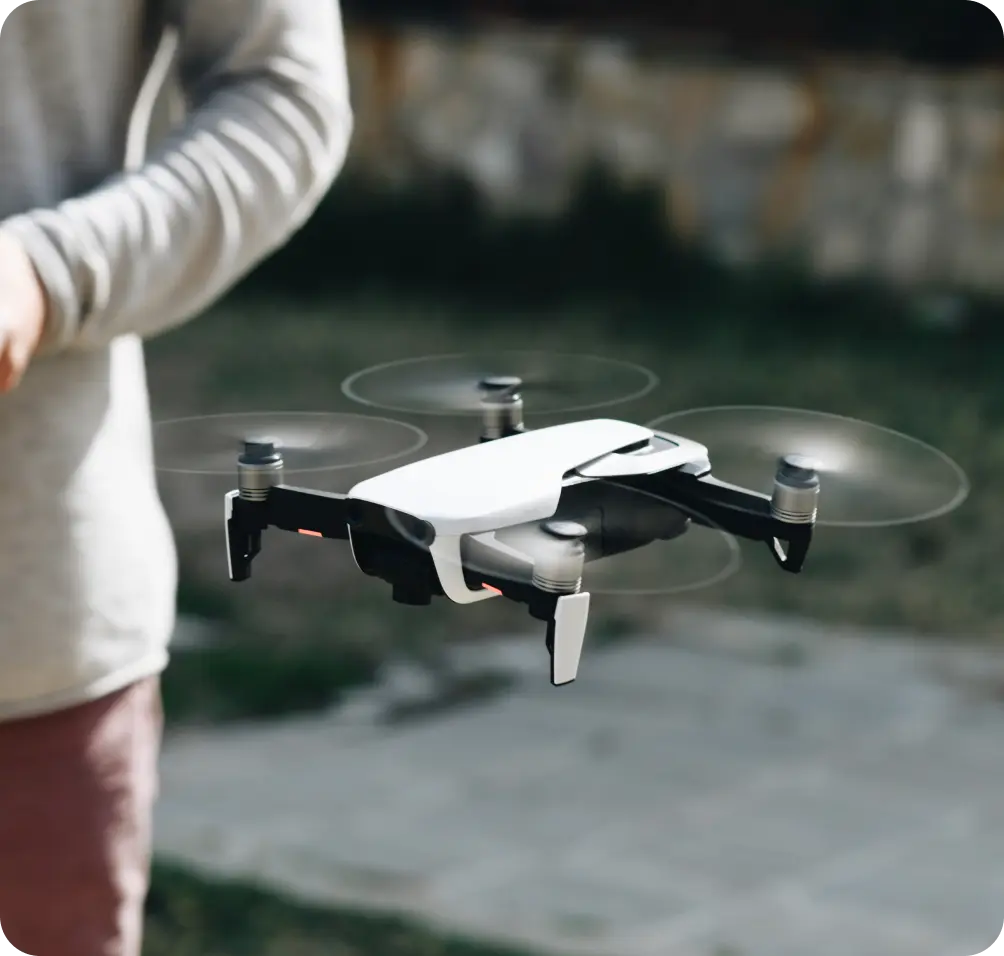 A close-up of a drone en route to its drone docking station, with a person standing nearby in an outdoor setting.