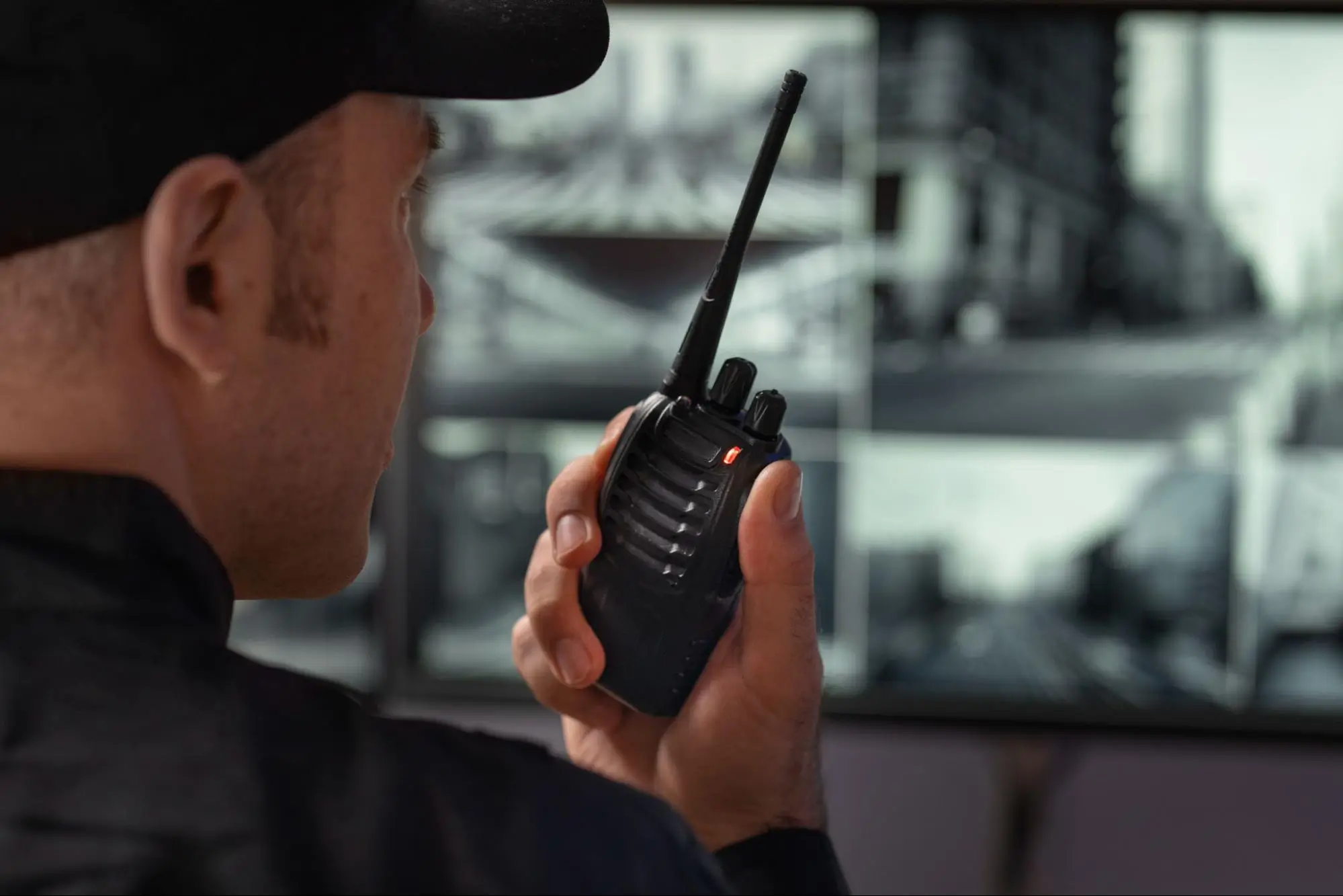 Professional security guard using two-way radio while monitoring live surveillance cameras in a security control room, providing rapid response services by American Security Force.