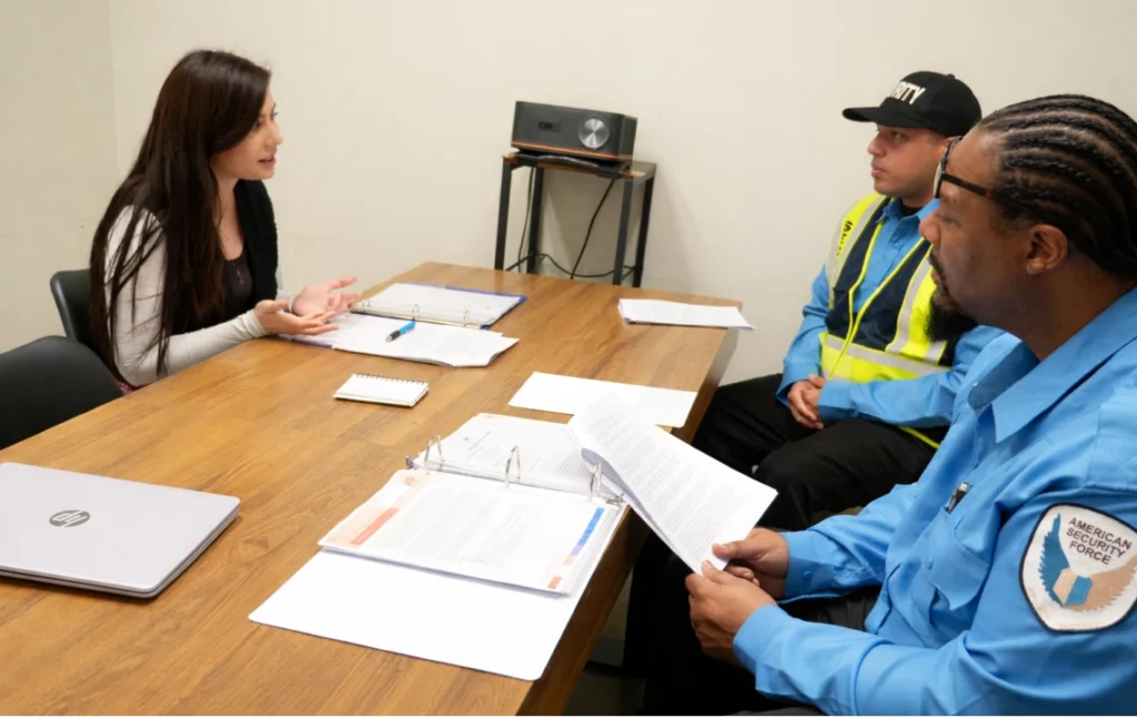 Security Guard Hiring & Training Consultation | American Security Force American Security Force supervisor interviewing security guards during hiring or training meeting with documents