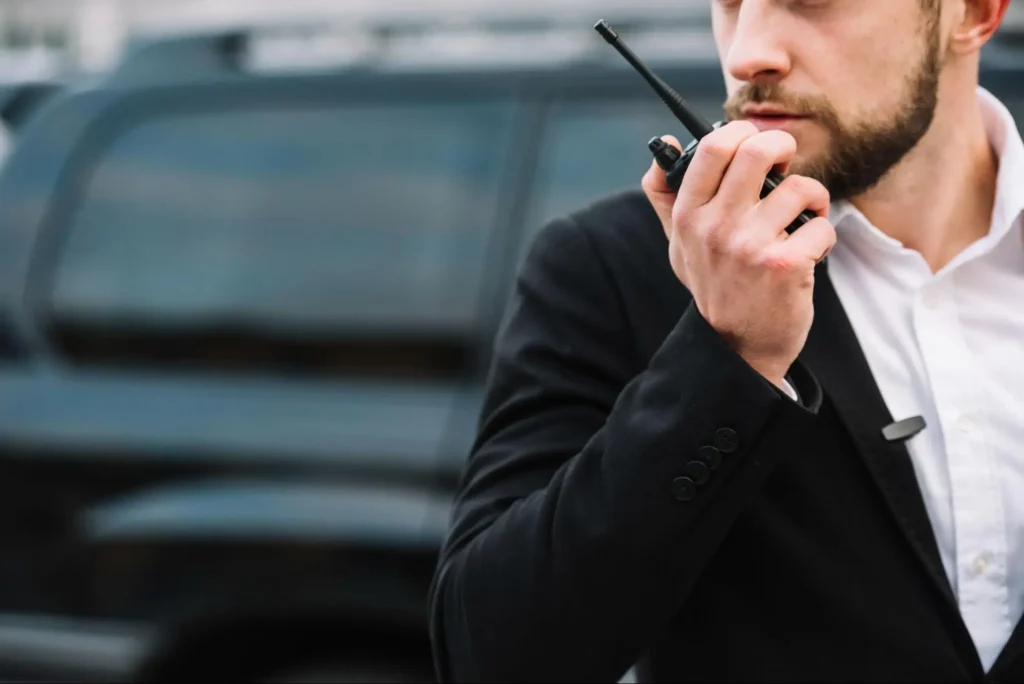 Executive Protection Security Agent | American Security Force Executive protection security agent using a radio near a vehicle for American Security Force